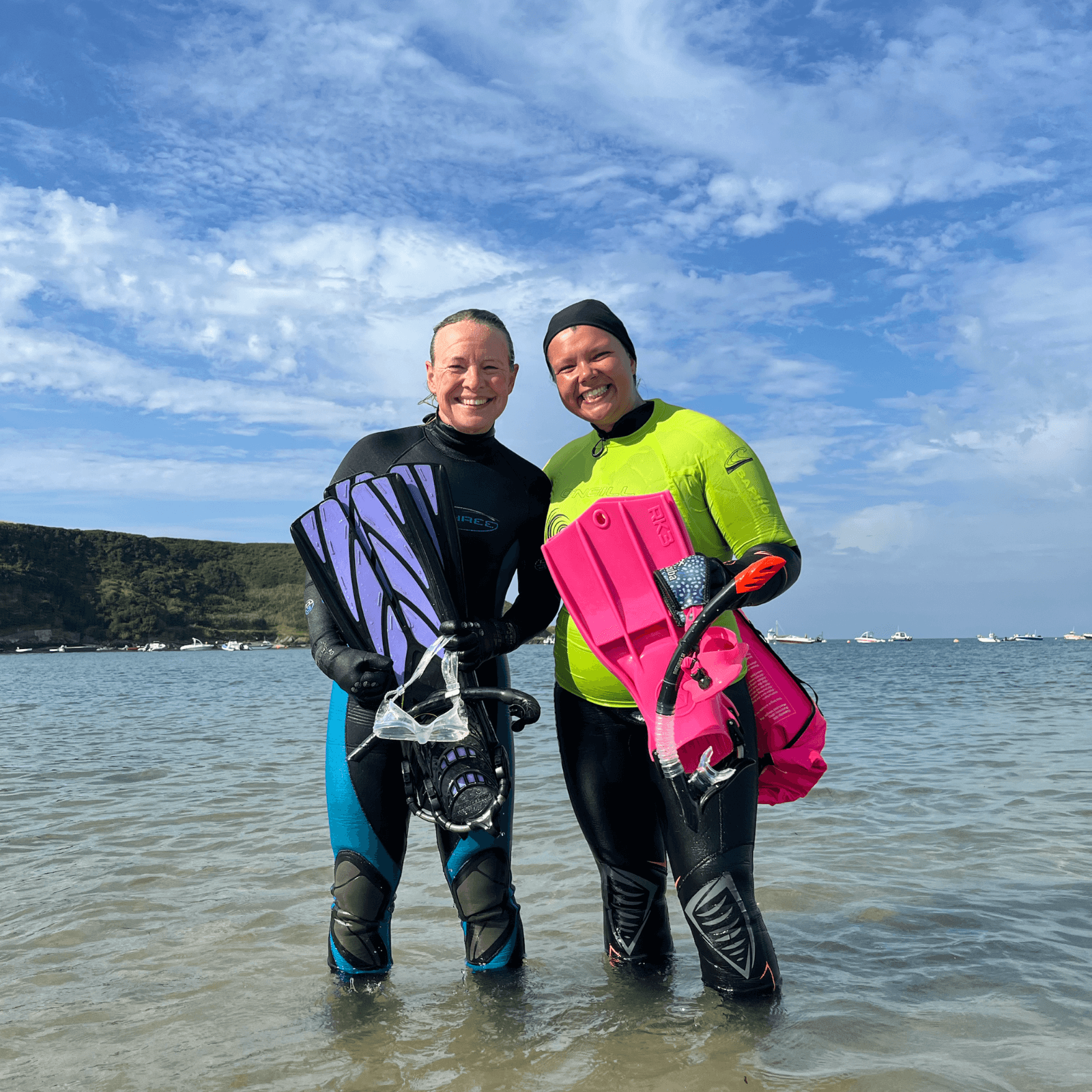 Project Seagrass Ambassador Miranda and North Wales Project Assistant Amel are standing in the water to just below knee height. They are holding their flippers following a snorkel to collect seagrass seeds.