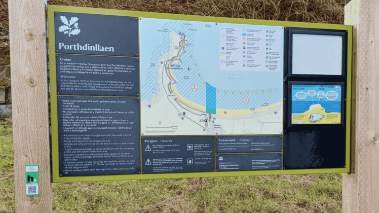 An information board with information about Porthdinllaen in North Wales. On the left hand pillar of the board is a QR code where users can scan to receive further information about the seagrass meadow in Porthdinllaen.