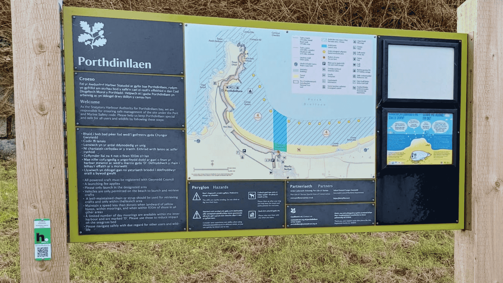 An information board with information about Porthdinllaen in North Wales. On the left hand pillar of the board is a QR code where users can scan to receive further information about the seagrass meadow in Porthdinllaen.