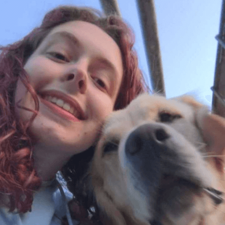 Abi's head is leaning against her dog's head. She has red curly hair.