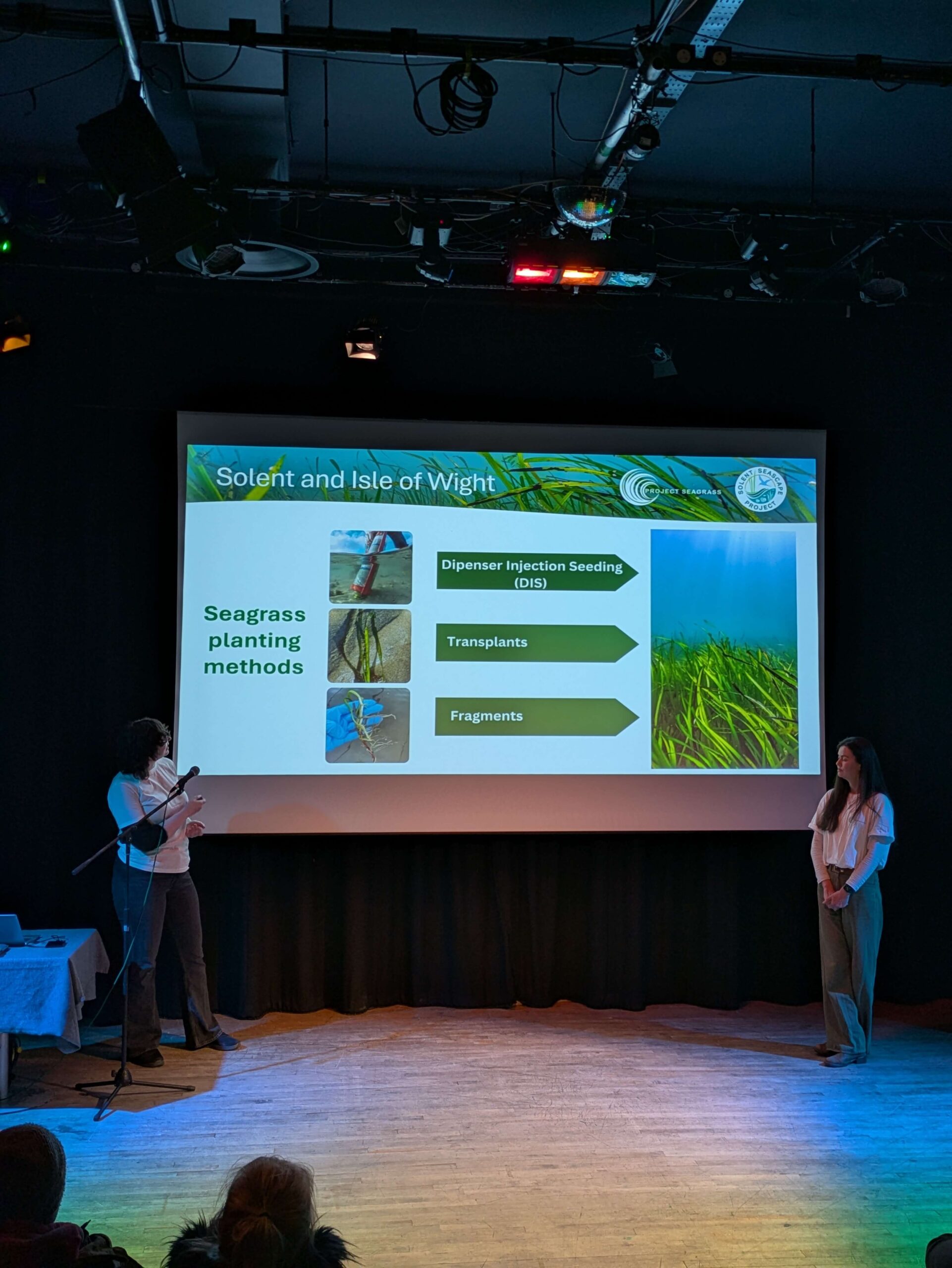 Emma and Anouska stand either side of a projector as they deliver a presentation of seagrass in the Isle of Wight.