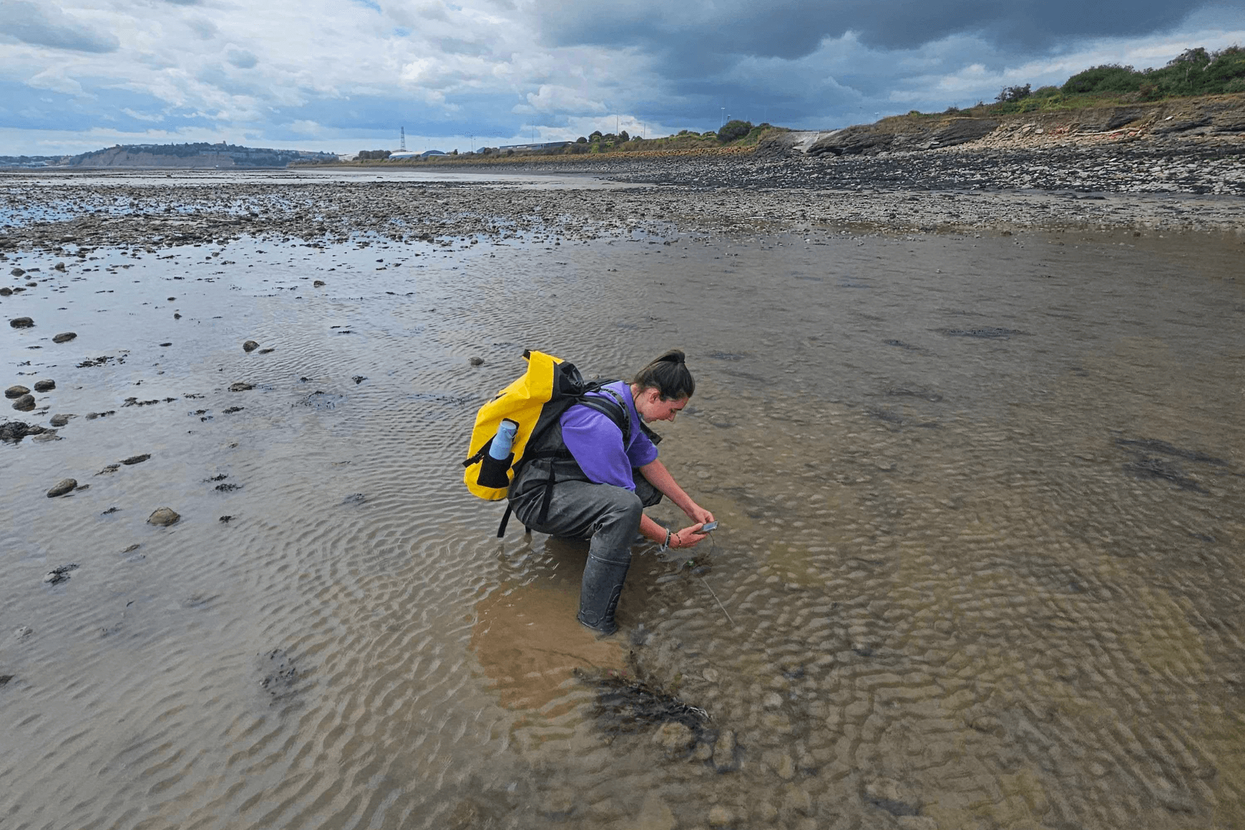 Emma is crouching on the beach in Cardiff carrying out monitoring work.