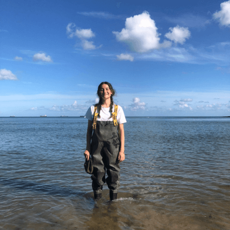 Anya is standing in the sea whilst out on fieldwork. She is wearing green waders.