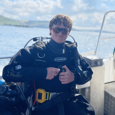 Ewan is aboard a boat. He is wearing dive gear. The sun is shining.
