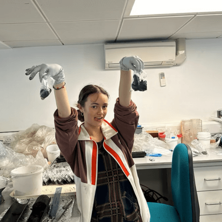 Grace is standing in a lab holding bags of samples.