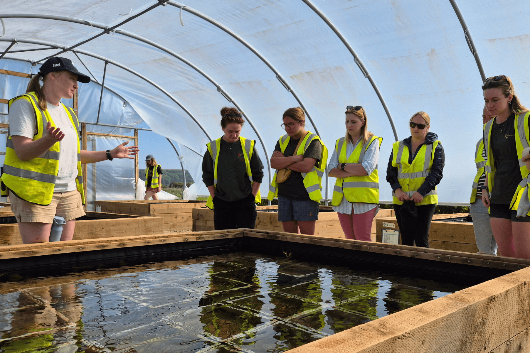 Nursery Lead Emily Yates is delivering a tour of the Seagrass Nursery. Visitors and Emily are all wearing high vis jackets.