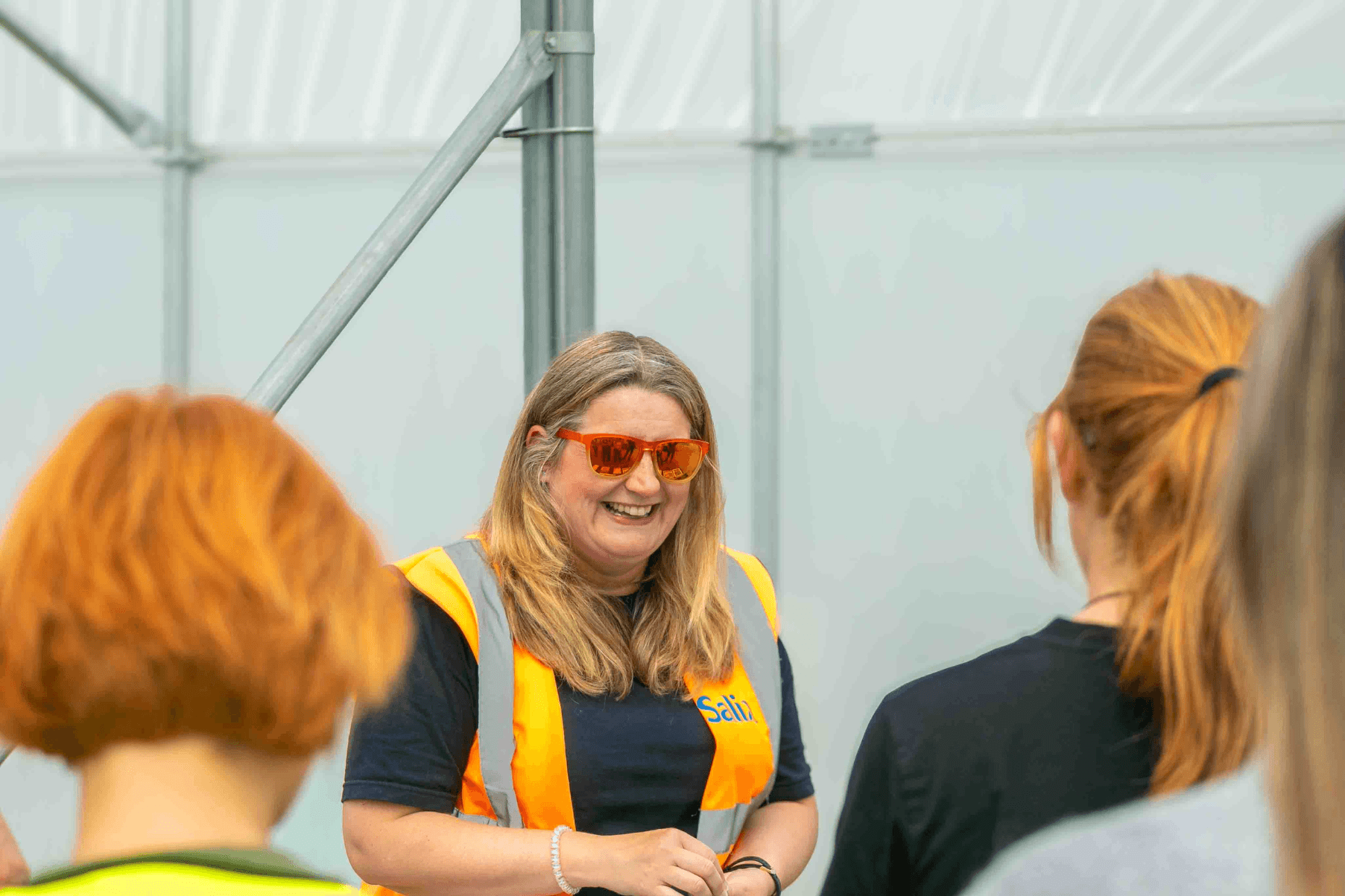 Katie is wearing an orange high vis jacket. She is speaking to a group of visitors at the Open Day.