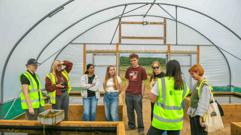 A group of people are gathered around a pond inside one of the Seagrass Nursery polytunnels