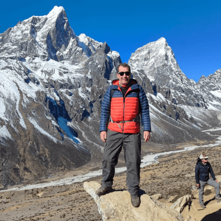 Mark is standing in a mountain range. He is wearing hiking clothes.