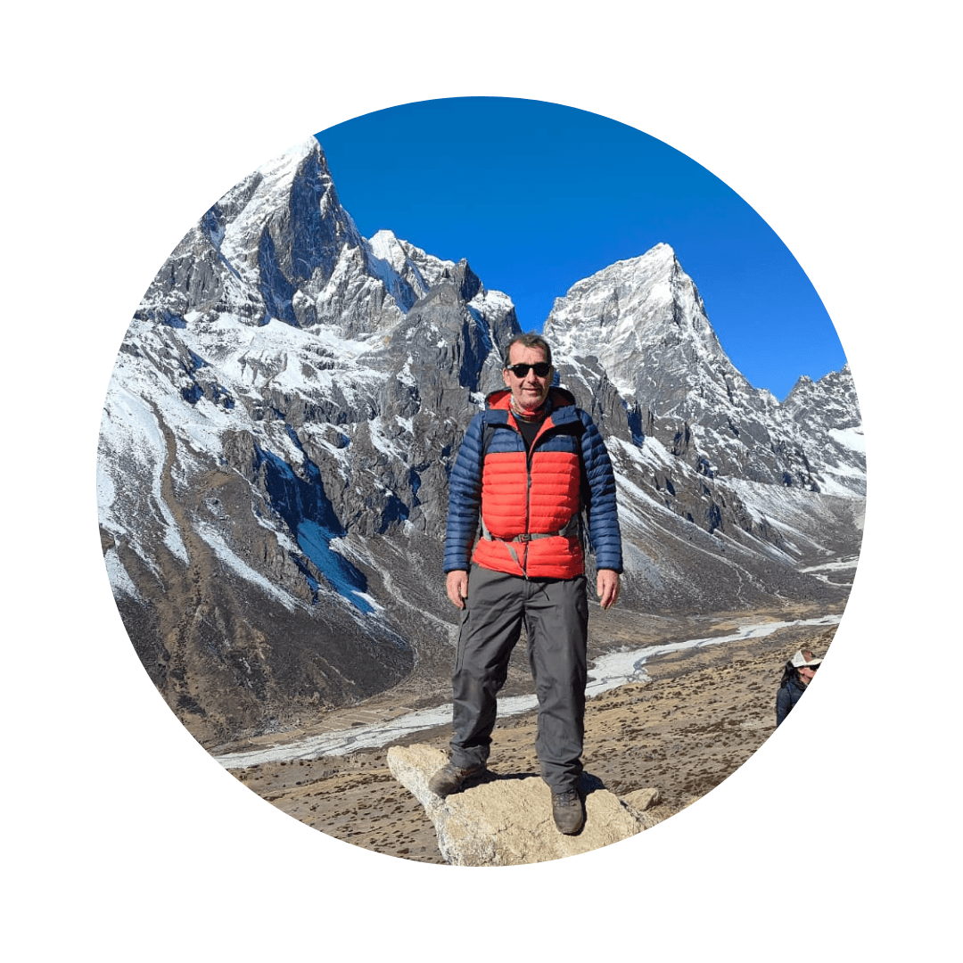 Mark is standing in a mountain range. He is wearing hiking clothes.