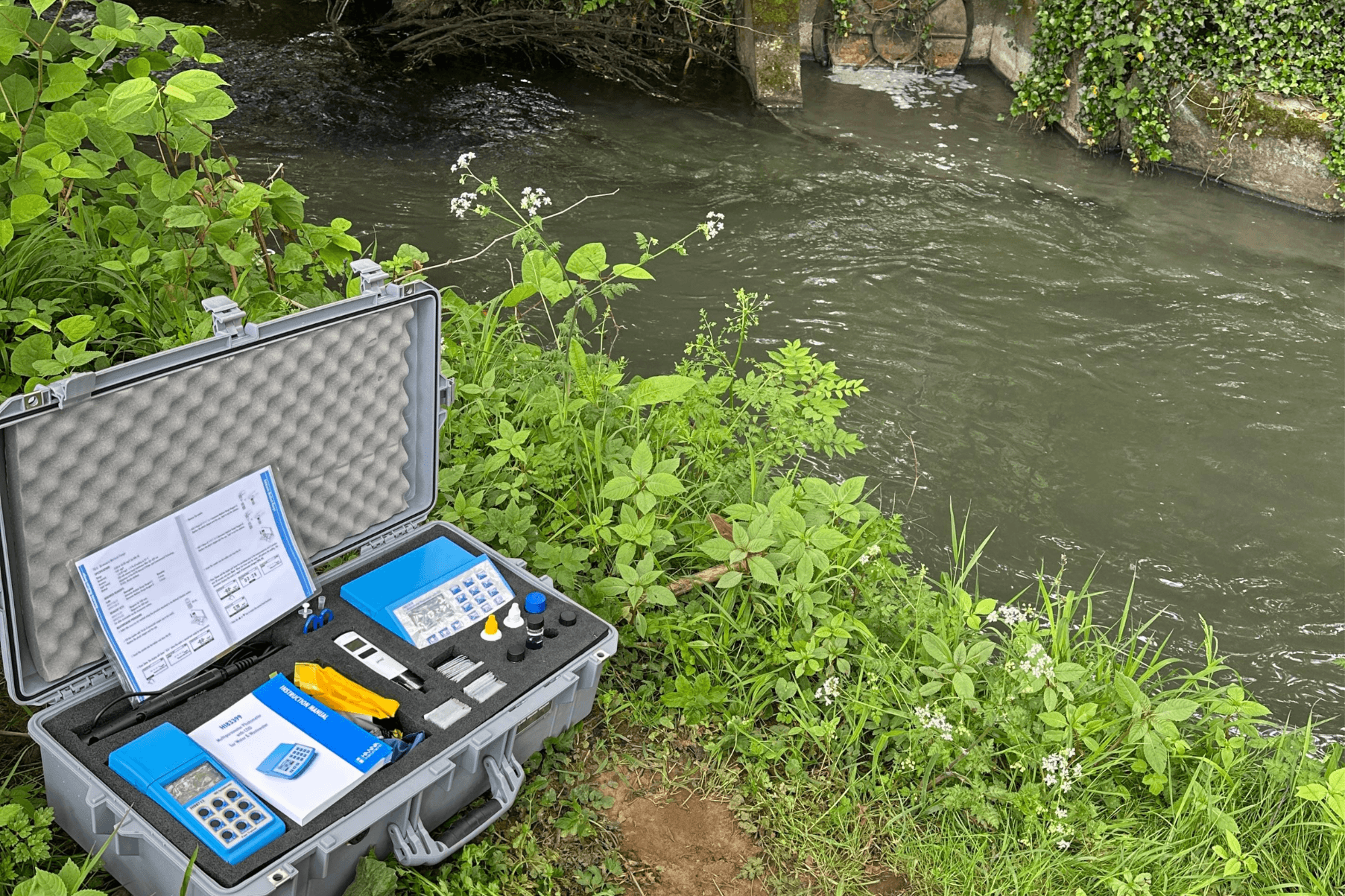 A box of monitoring equipment is on the riverbank of the Afon Cynffig Kenfig River