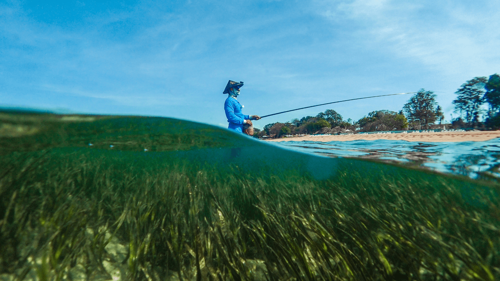A fisher stands in the sea with a fishing rod.