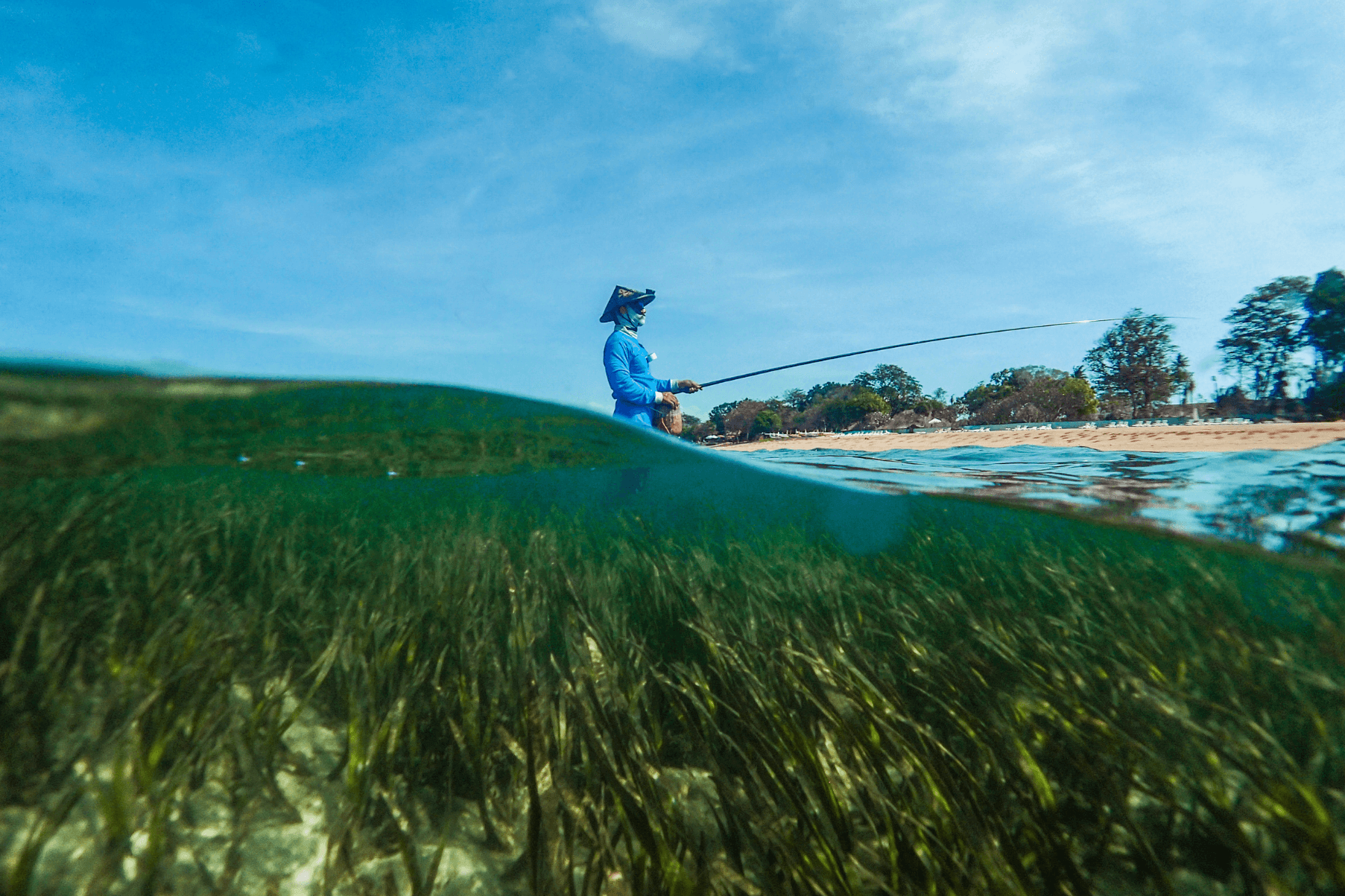 A fisher stands in the sea with a fishing rod.