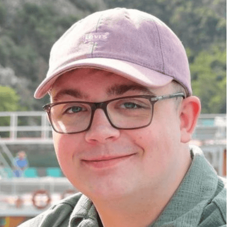 Ieuan is wearing a light coloured cap. He is wearing glasses and a green polo-neck t-shirt.
