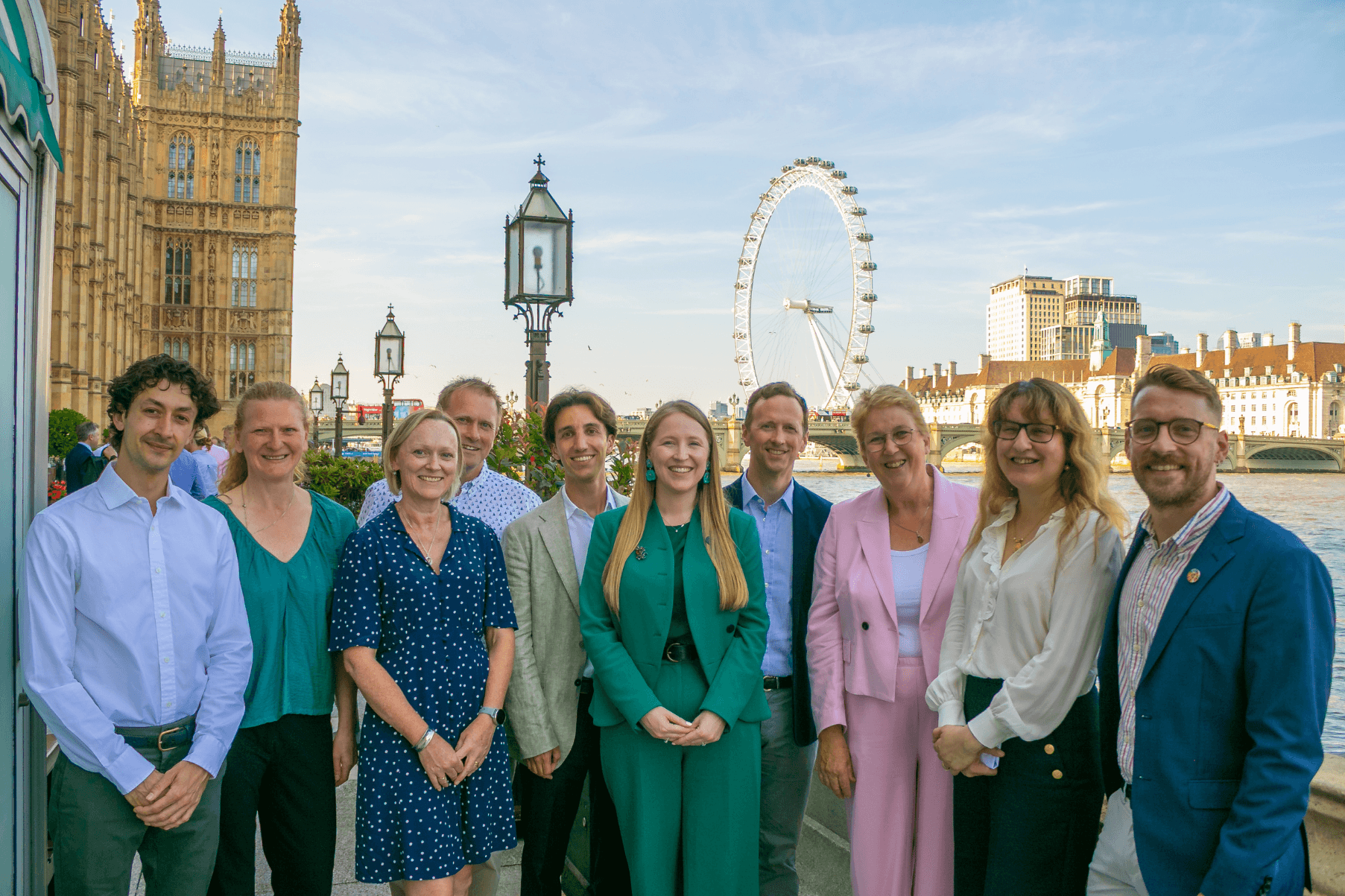 A group ten people stand outside Westminster with the London eye in the background. They are dressed smartly for a parliamentary event .