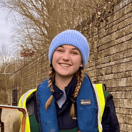 Megan is wearing a high vis jacket and a light blue hat. She was two plaits.