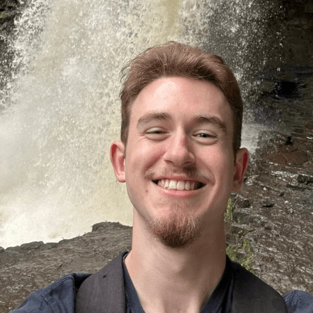 Billy is standing in front of a waterfall. He has light brown hair.