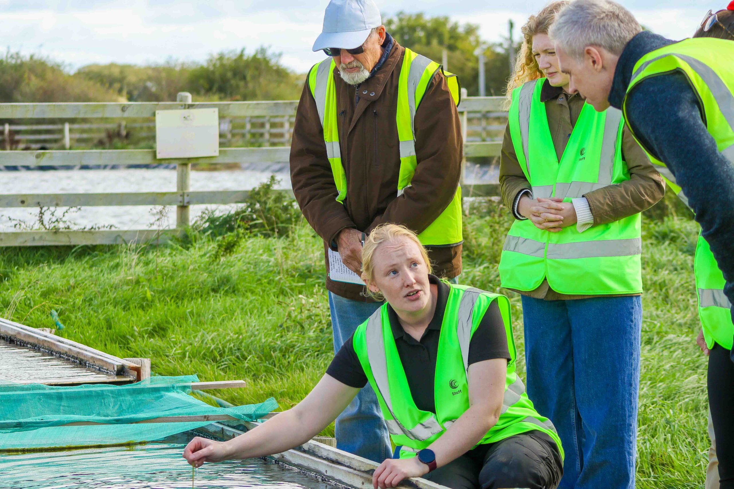 Emily Yates Nursery Manager is crouching beside the Oyster Ponds showing visitors.