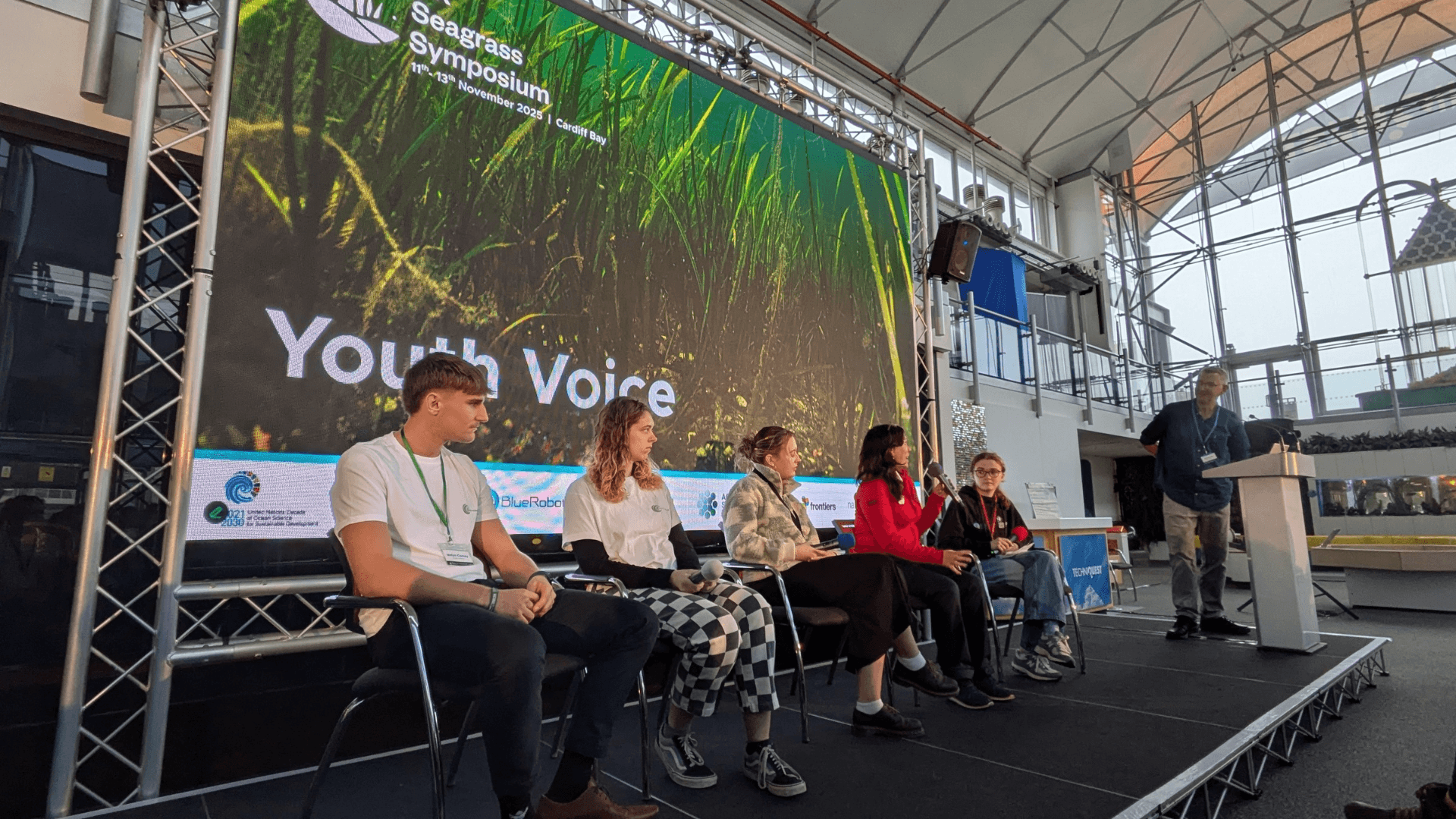 Five young people are seated on the stage at the UK Seagrass Symposium as part of the Youth Voice session.