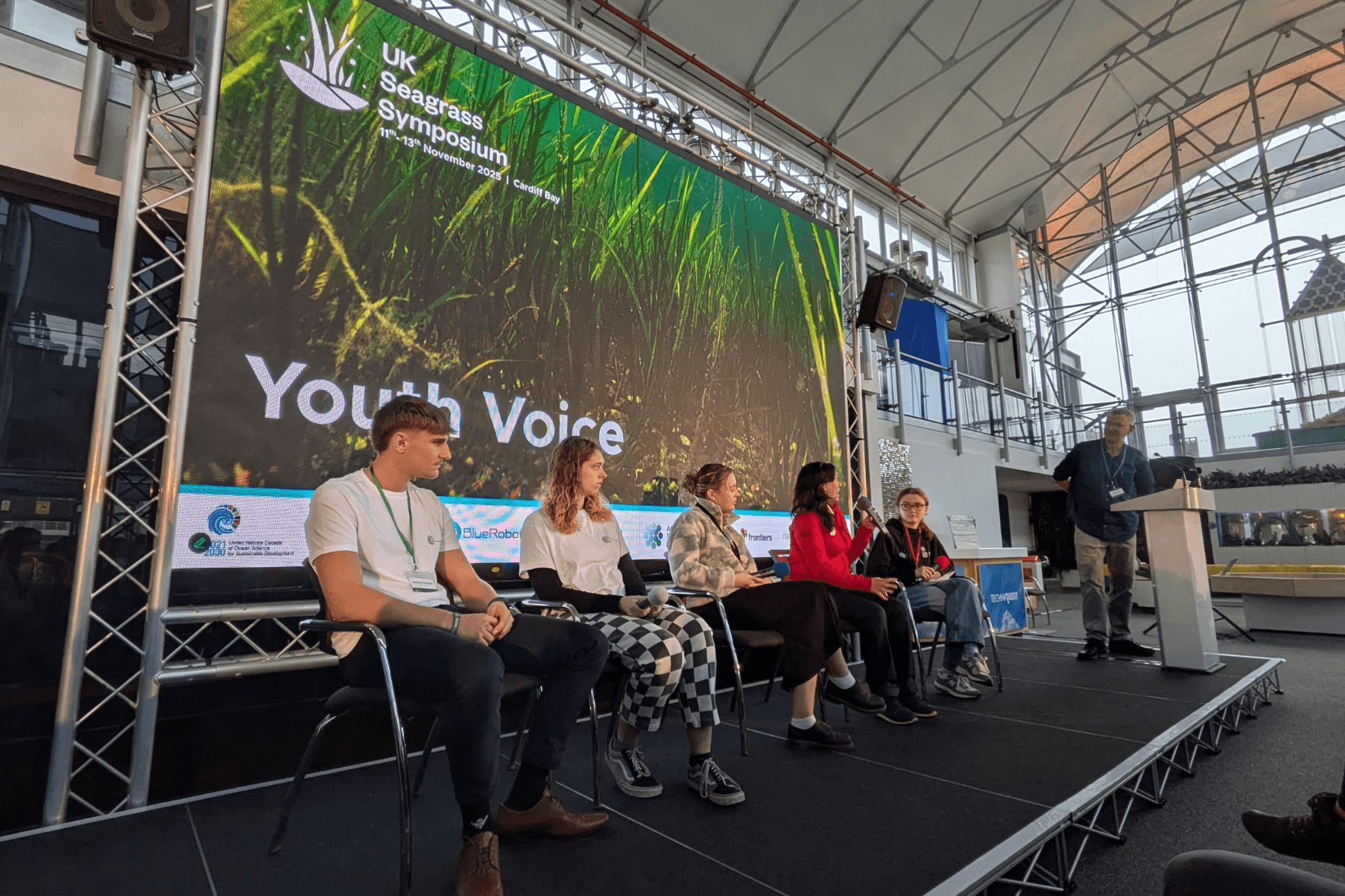 Five young people are seated on the stage at the UK Seagrass Symposium as part of the Youth Voice session.